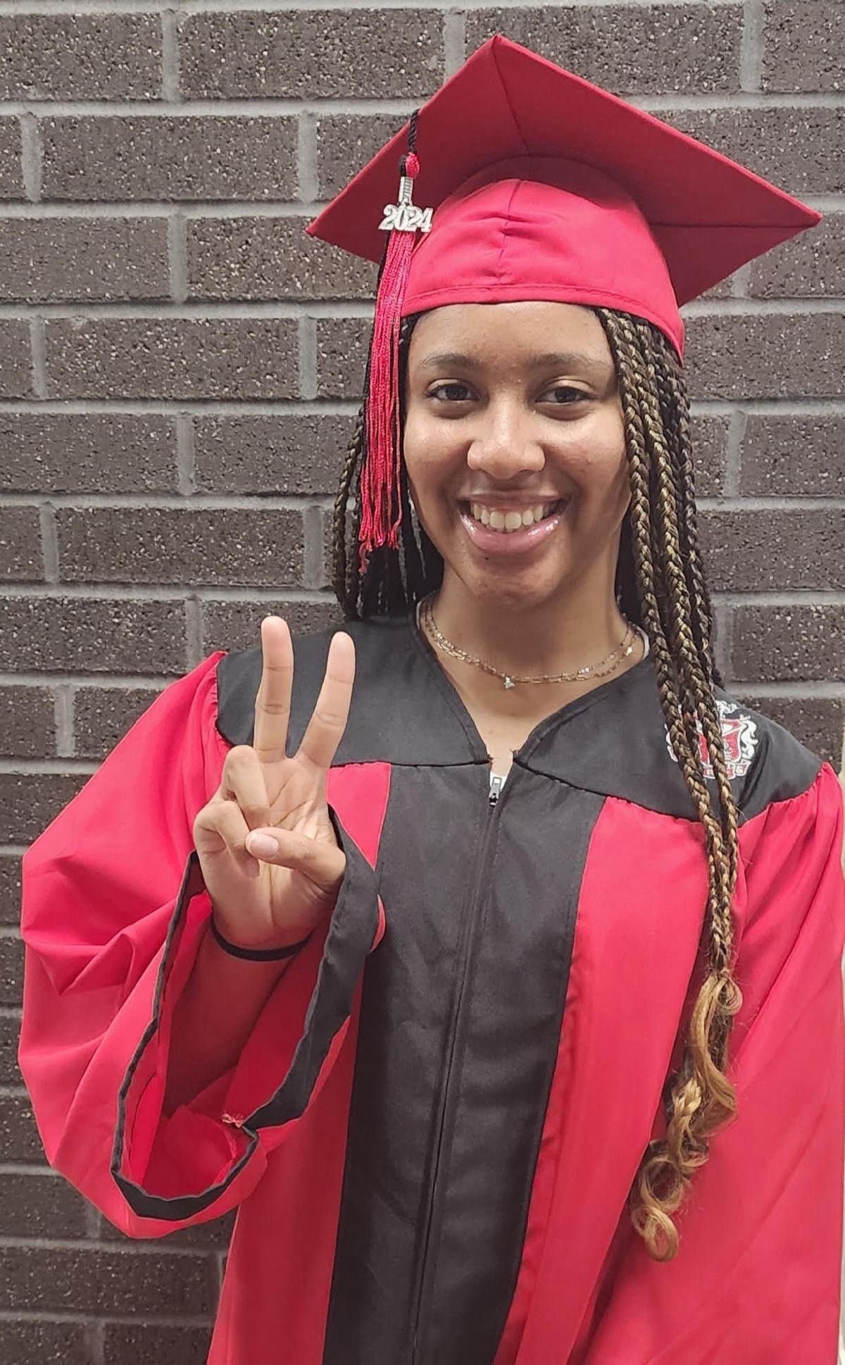 A woman in a red graduation cap and gown is giving a peace sign.