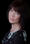 A woman with dark hair and bangs is wearing a black and white dress and looking at the camera.