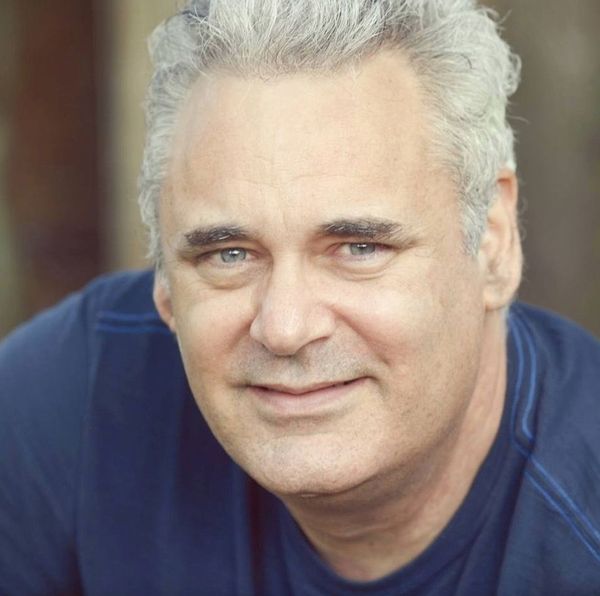 A man with gray hair is wearing a blue shirt and smiling