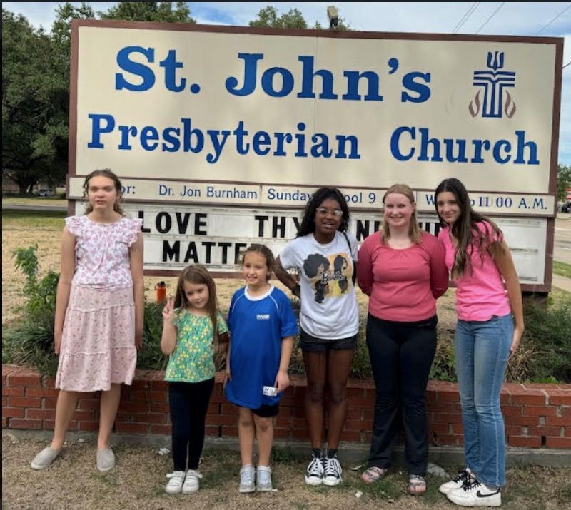 A group of girls standing in front of a sign for st. john 's presbyterian church