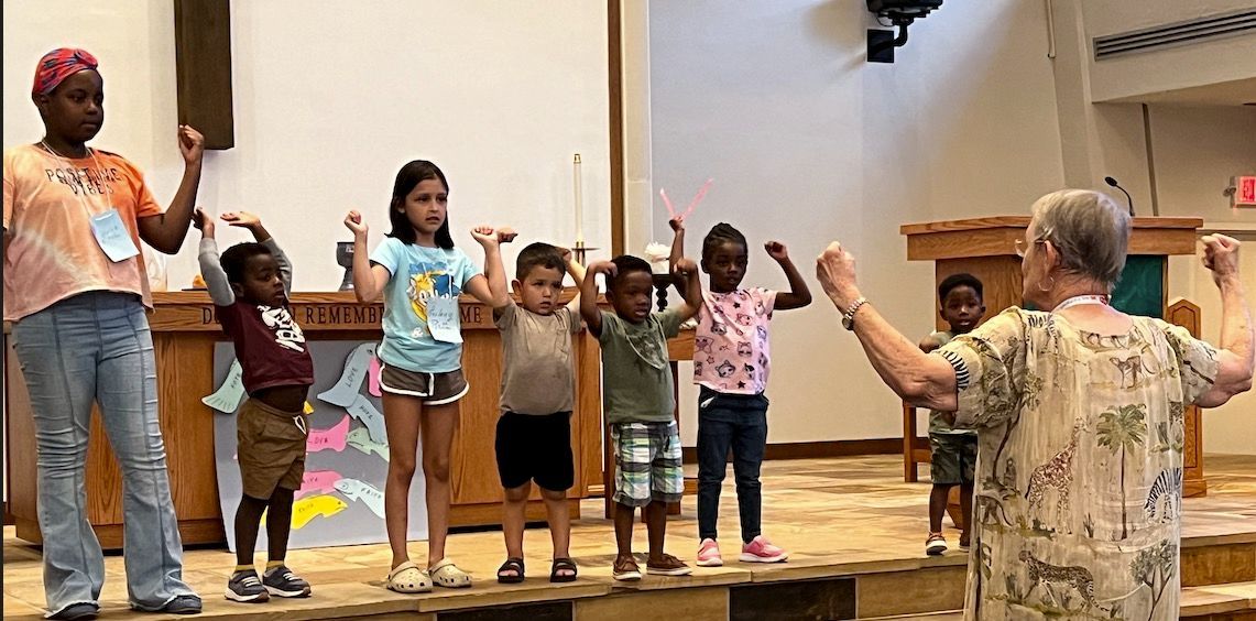 A group of children are standing on a stage with their hands in the air.