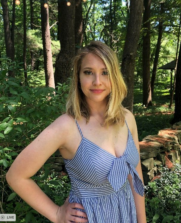 A woman in a blue and white striped dress is standing in the woods.