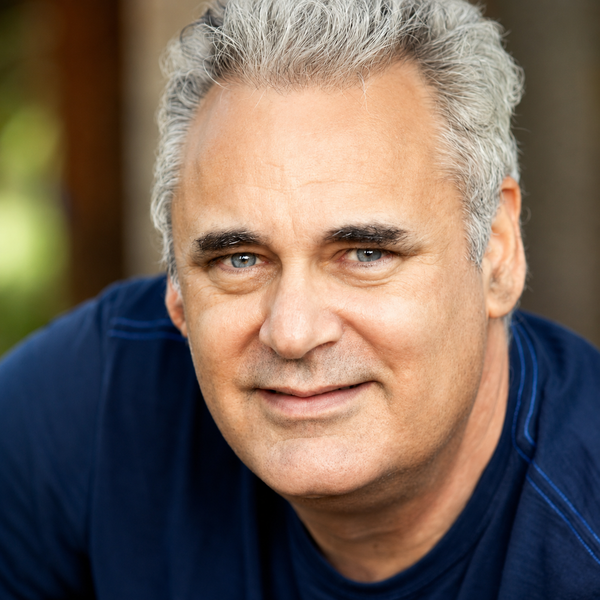 A man with gray hair is wearing a blue shirt and smiling