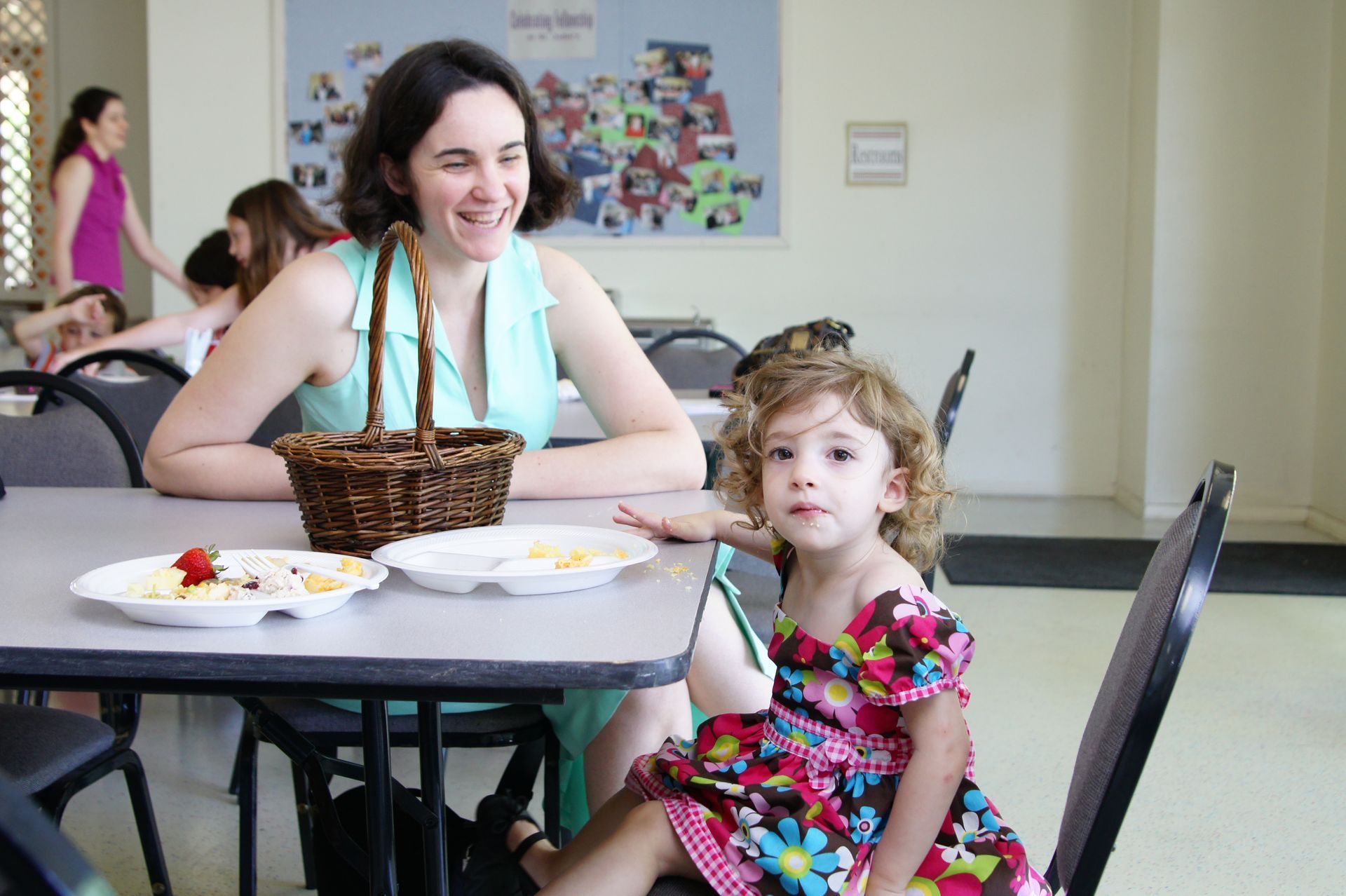 A woman and a little girl are sitting at a table with plates of food.