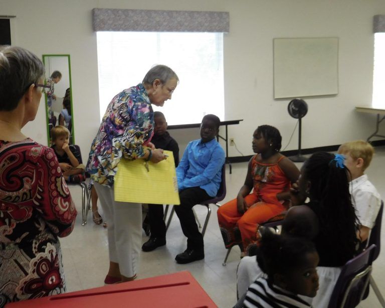 A group of people are sitting in chairs and a woman is holding a yellow piece of paper