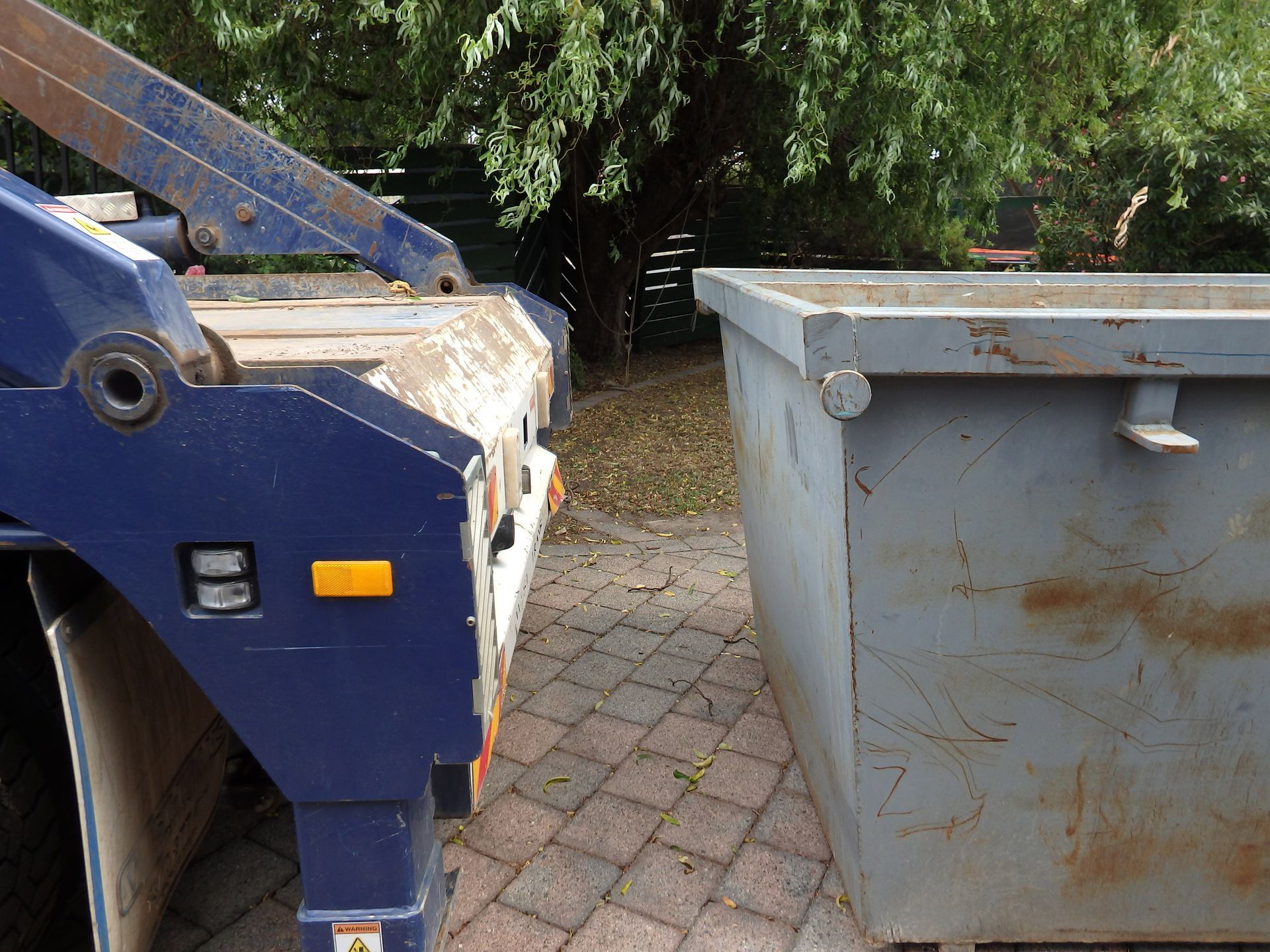 A close-up of a grey steel skip bin and truck for pick-up.
