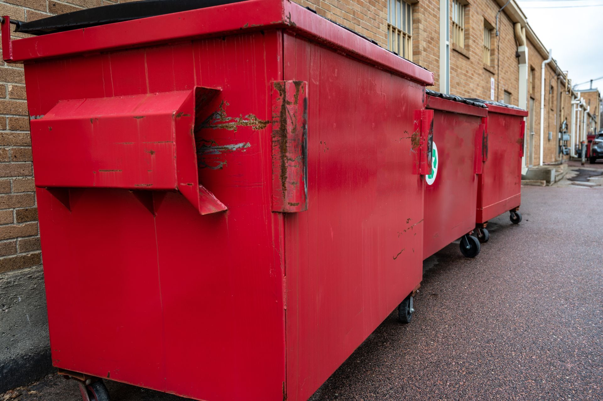 Multiple commercial rubbish bins lined up neatly against a brick wall.