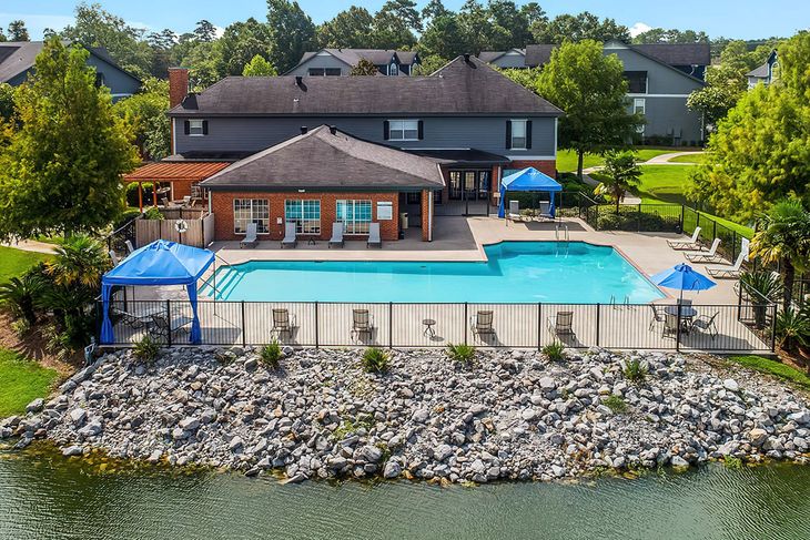 Pool area with building, lounge chairs, blue canopy, and lake.