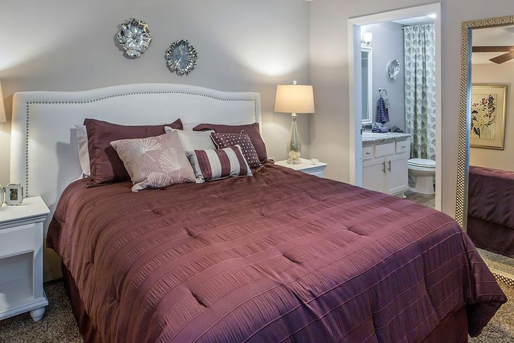 Bedroom with burgundy comforter, white headboard, and a mirror. White nightstands flank the bed.
