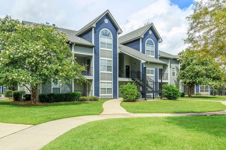 Apartment complex with blue and gray siding, green lawn, and a winding sidewalk.