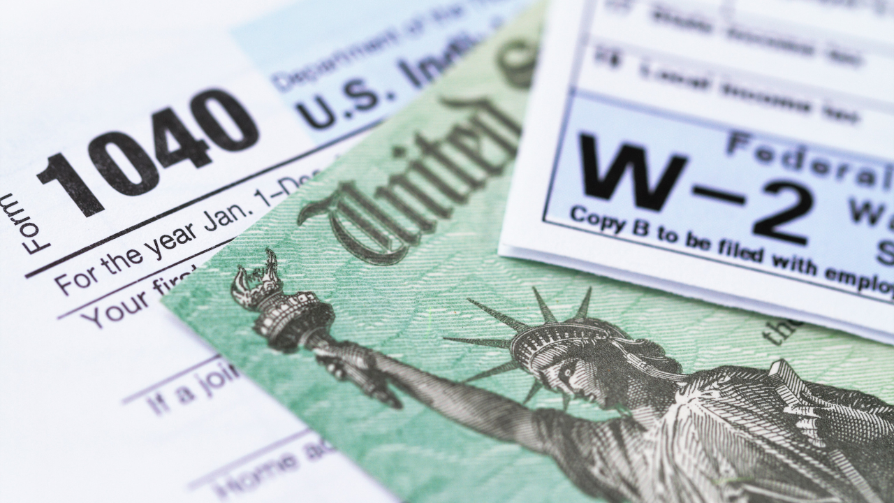 U.S. Form 1040 and a W-2 tax form placed under a green United States Treasury check featuring the Statue of Liberty.