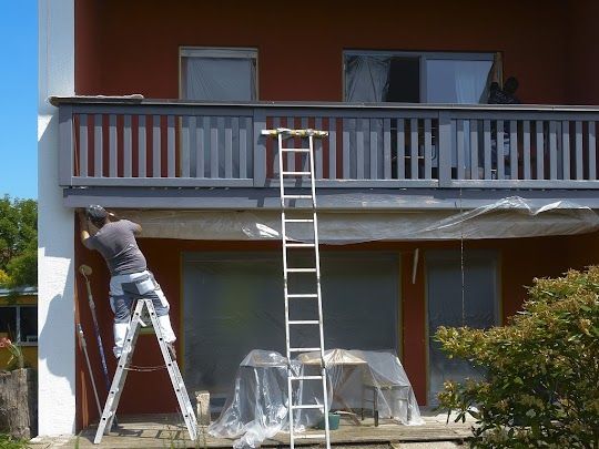 A man on a ladder is painting the side of a house