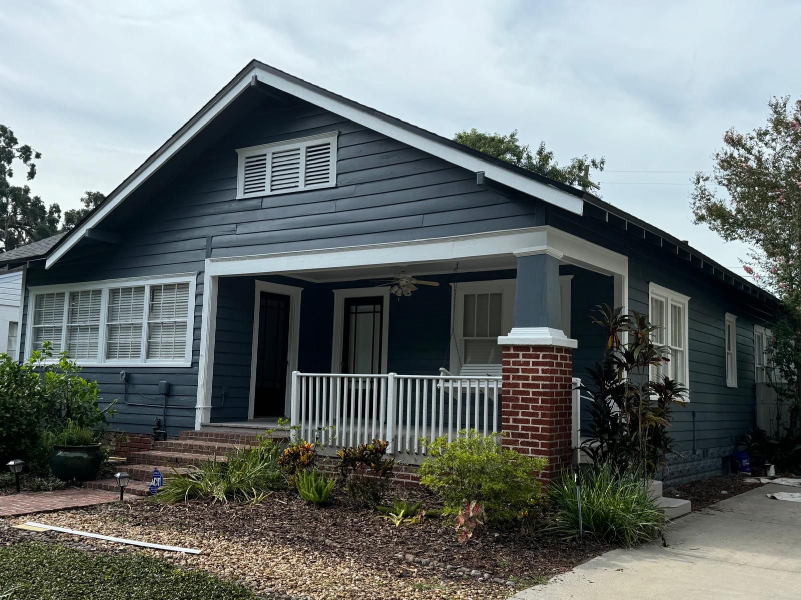 A blue house with a white porch and a brick pillar in front of it.