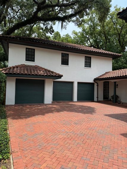 A white house with three garage doors and a brick driveway