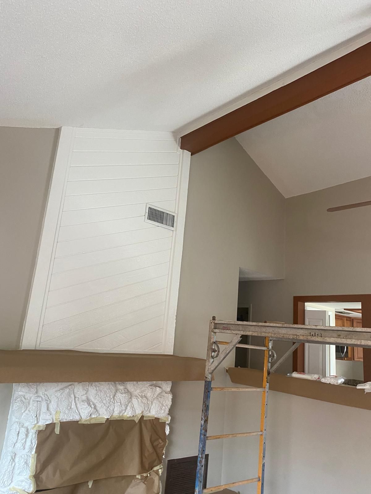 A fireplace is being painted in a living room with a ladder in the foreground.