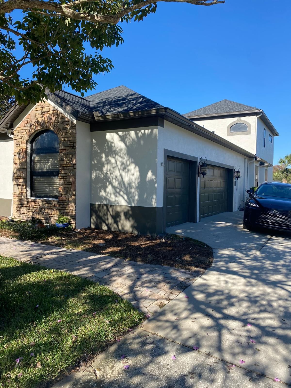 A car is parked in front of a house with two garages.