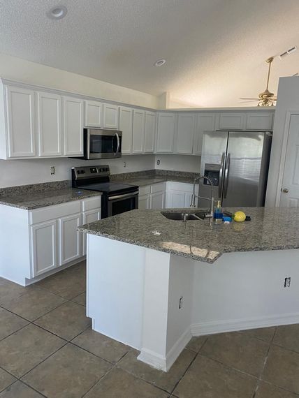 A kitchen with white cabinets , granite counter tops , stainless steel appliances and a large island.