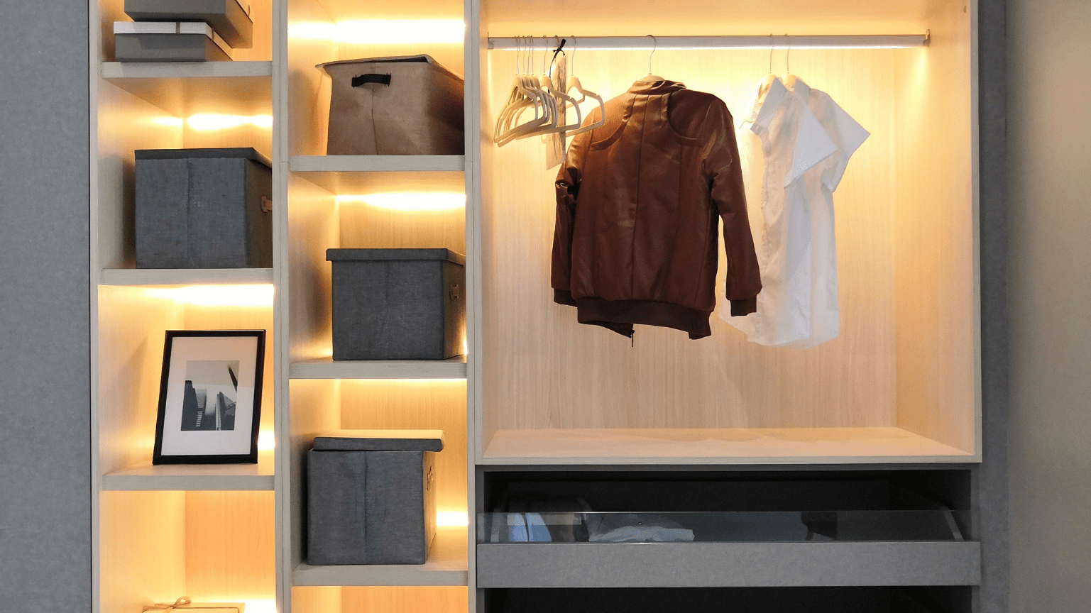 Built-in closet with shelves and hanging rod. Lit interior with gray bins, picture frame, and clothing — Intolec Electrical In Tweed Heads, NSW
