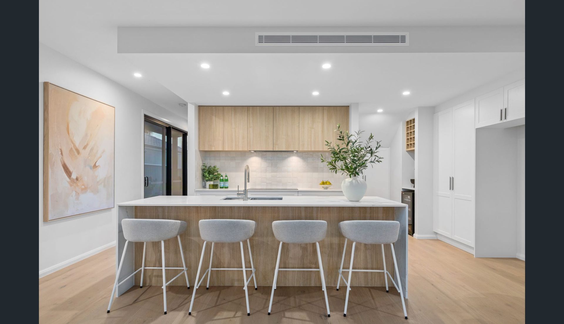 Modern Kitchen With Light Wood Cabinets, Island, and Bar Stools — Intolec Electrical in Tweed Heads, NSW