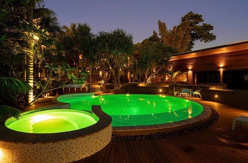 Green-lit pool and jacuzzi at night, surrounded by trees and wooden deck. — Intolec Electrical In Tweed Heads, NSW