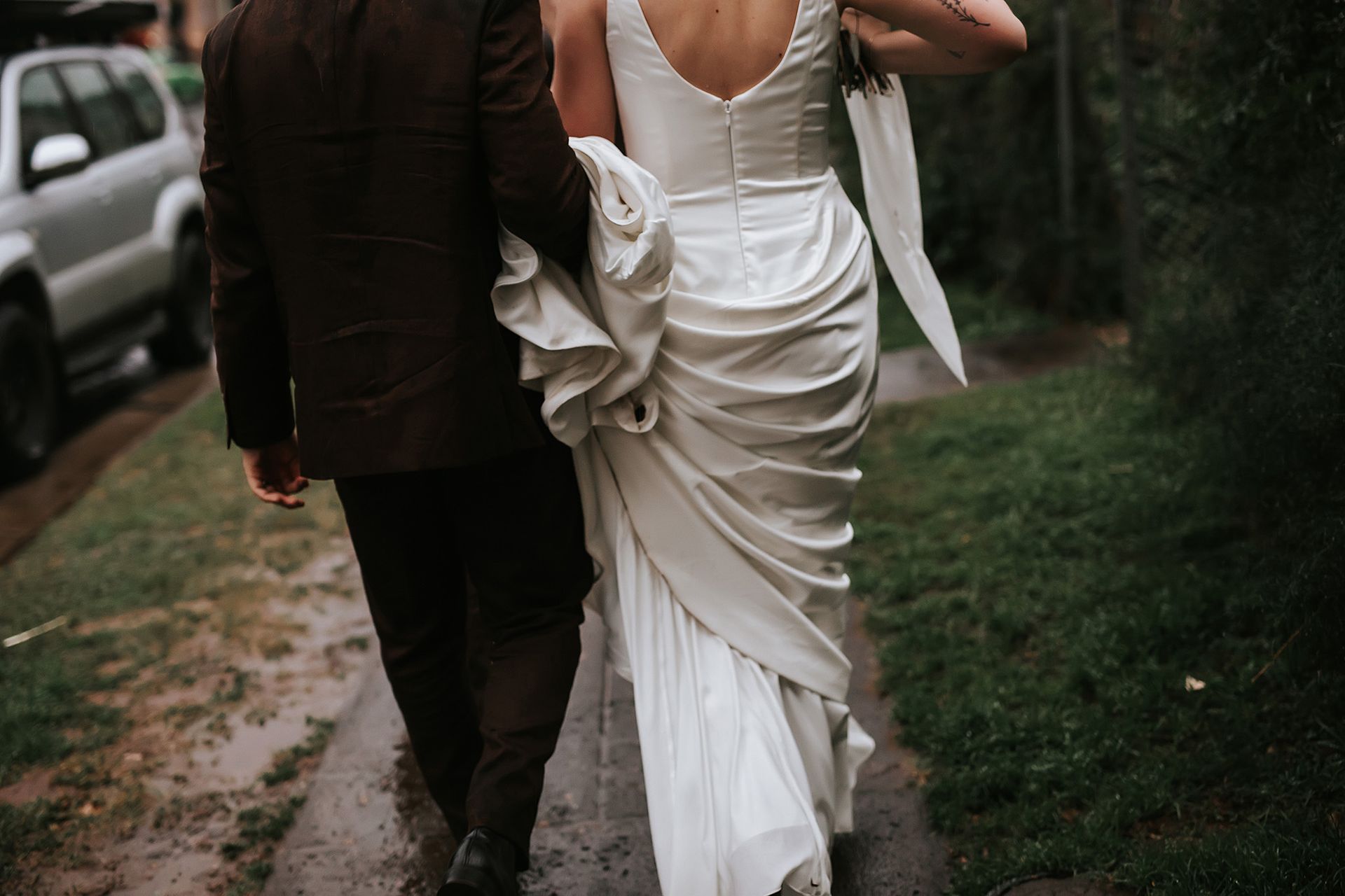 Bride and groom walking together on a wet path, the bride in a white gown and the groom in a dark suit.