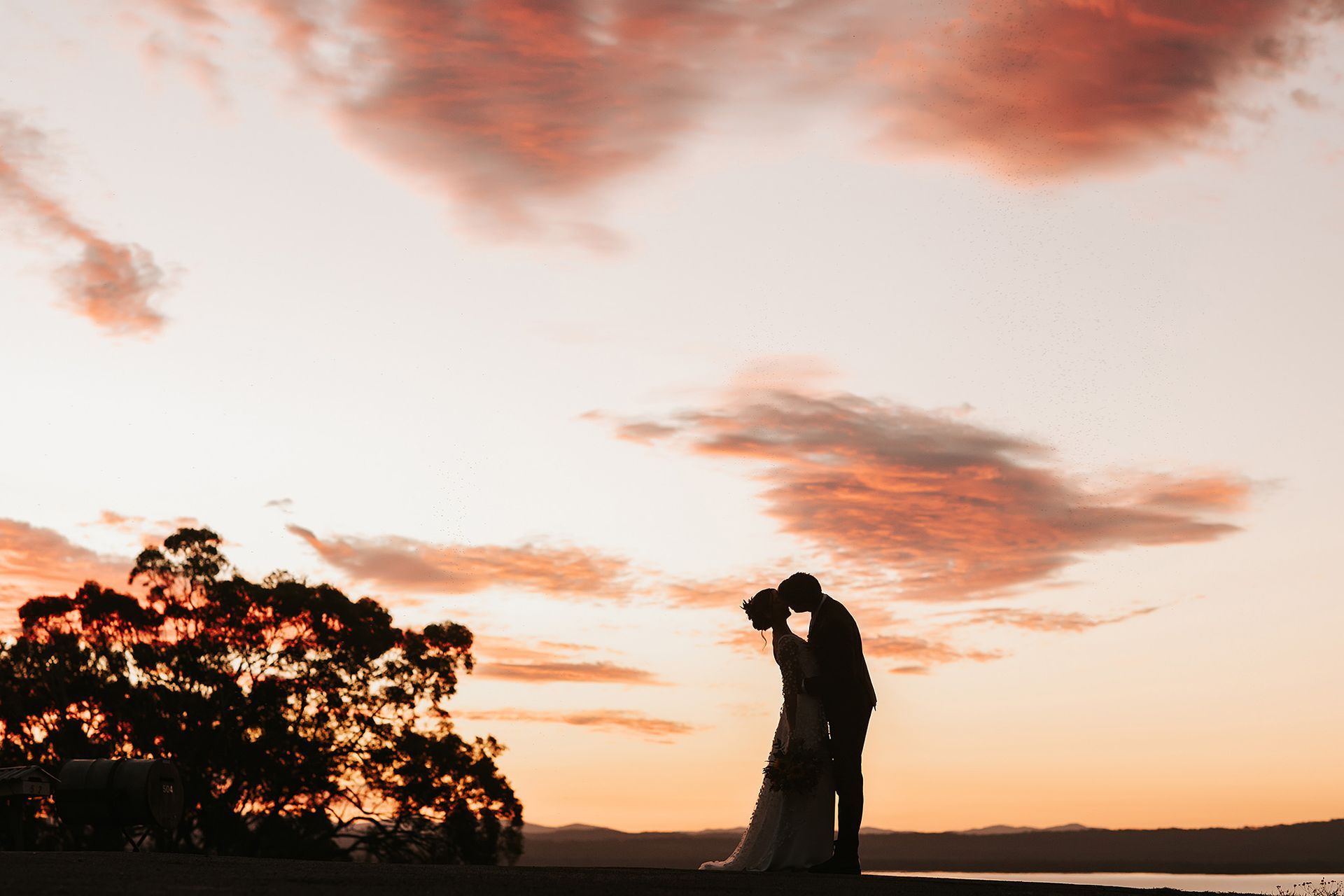 Couple kissing at sunset in Northern NSW, silhouetted against a peach and pink sky.