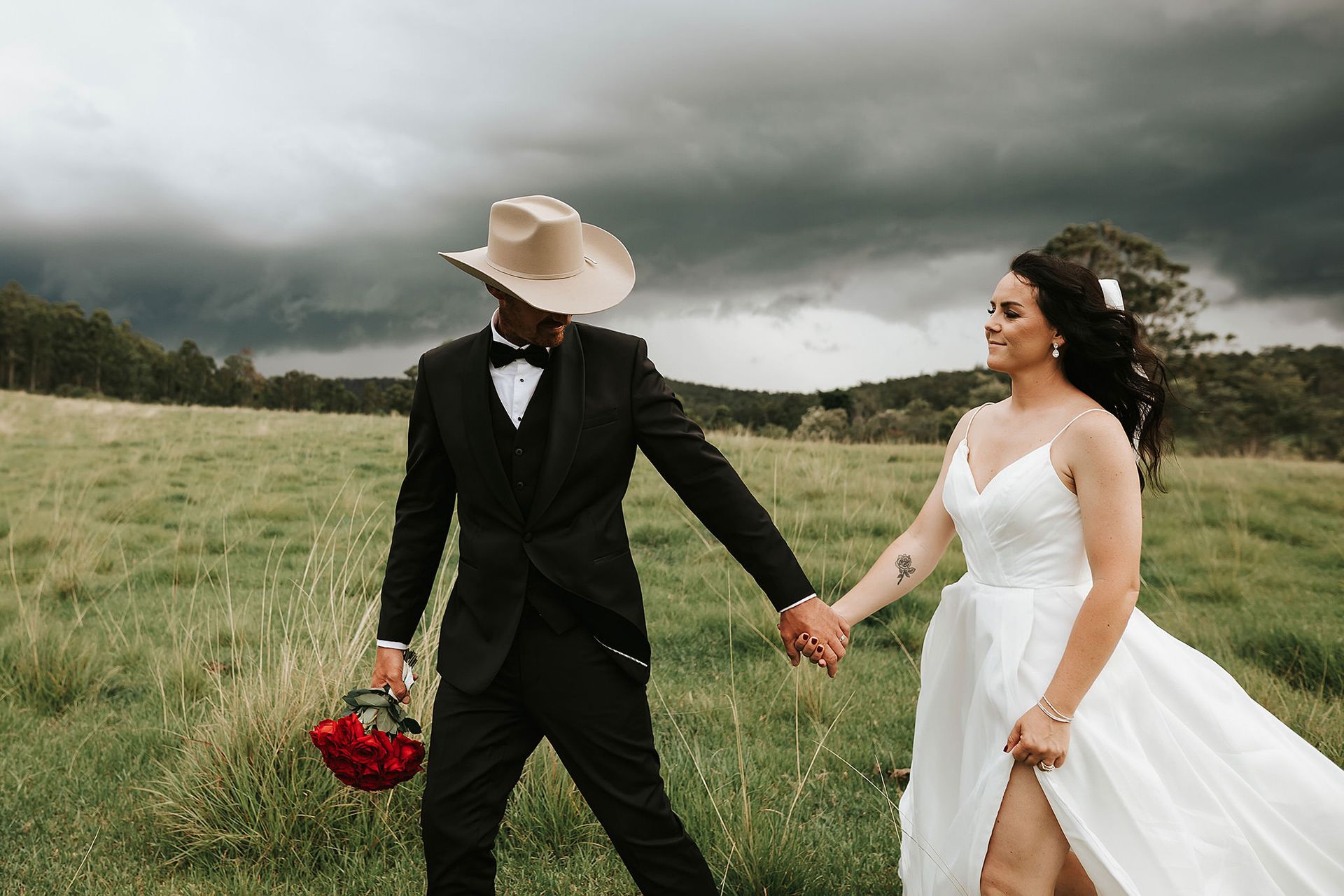 Couple in wedding attire hold hands in a field in Northern NSW with a cloudy sky.