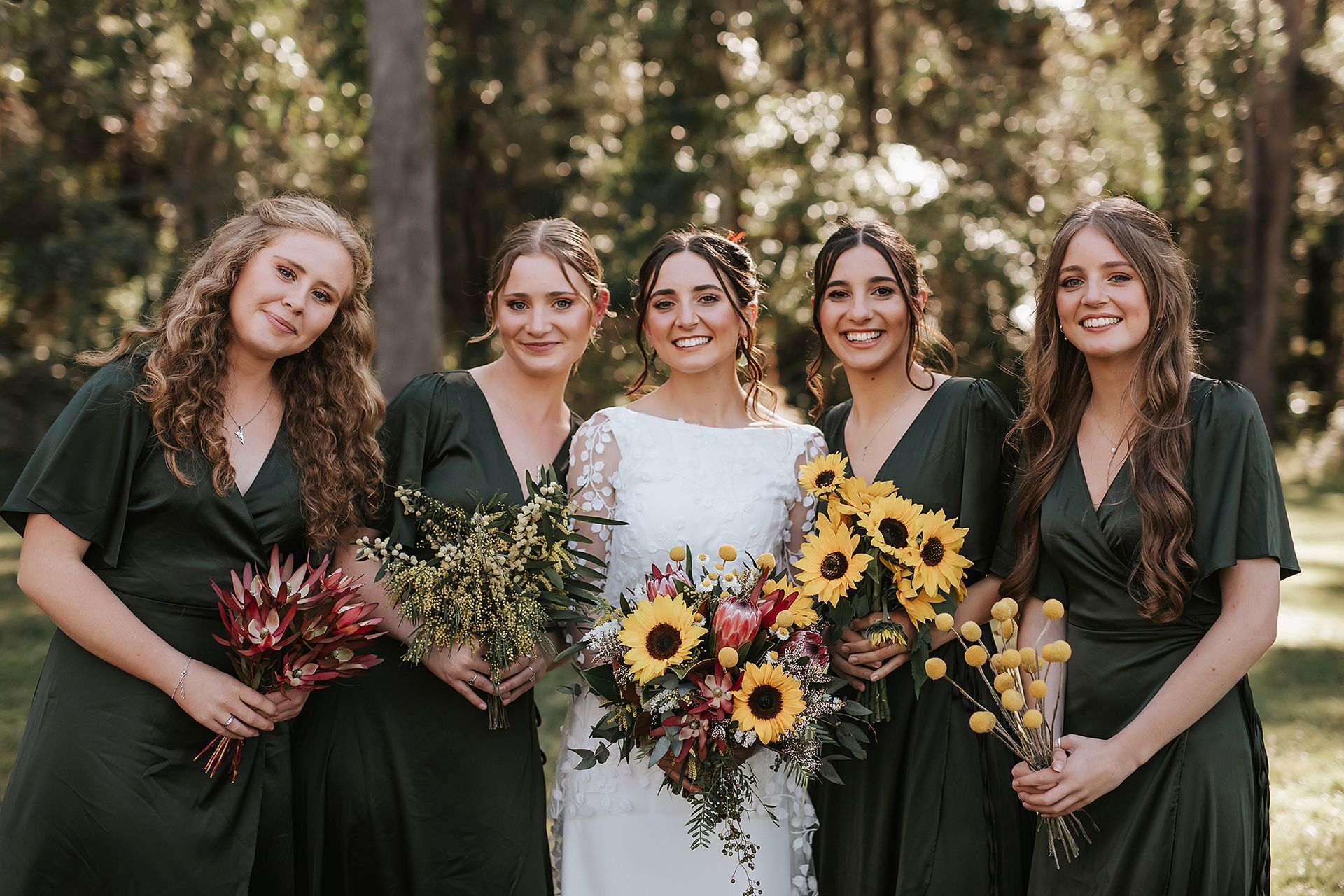 Bride and bridesmaids in a Northern NSW forest. Bride in white dress, bridesmaids in green dresses, holding bouquets.
