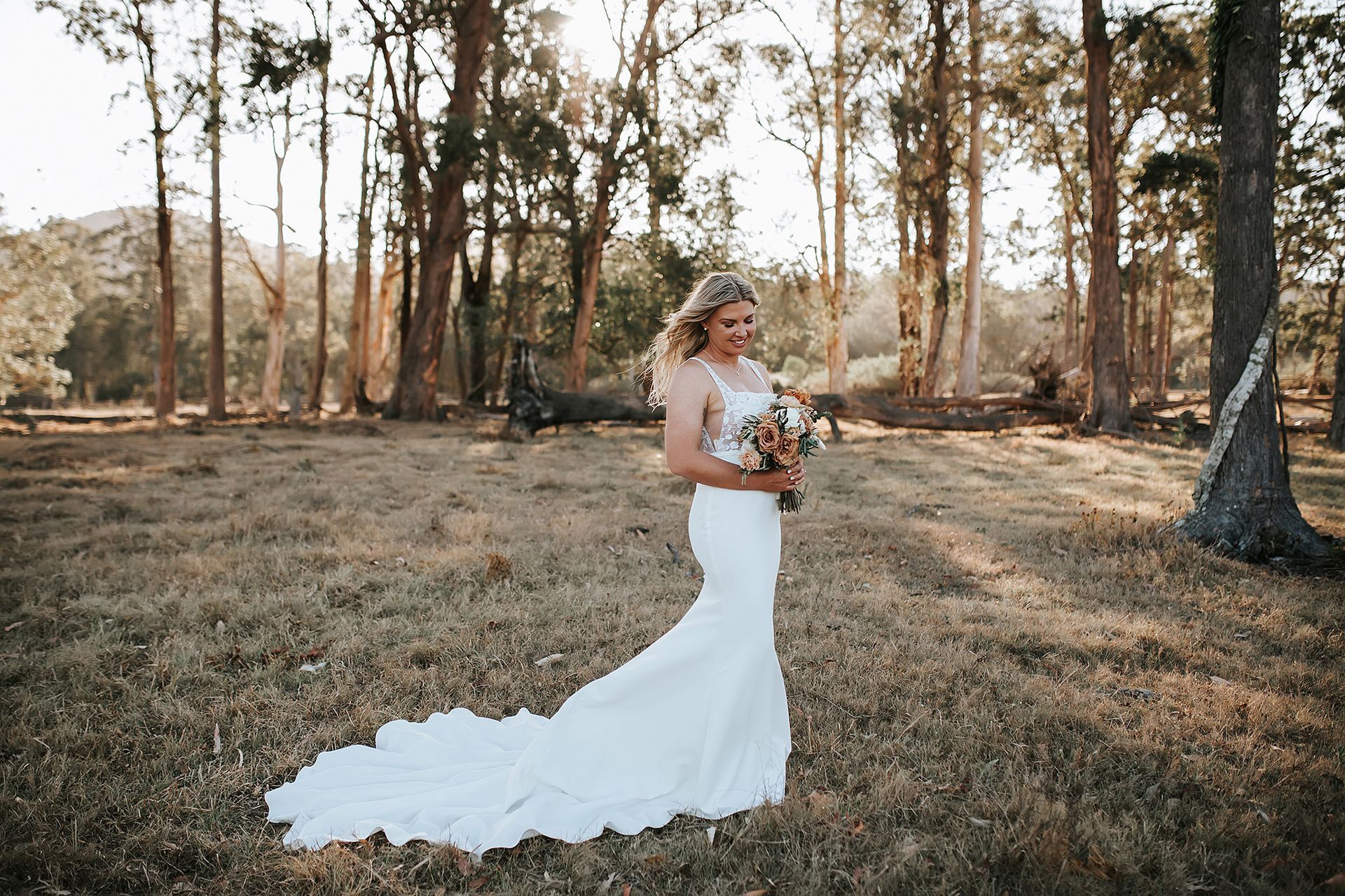 Bride in a white gown holding a bouquet, standing in a Northern NSW field with trees.