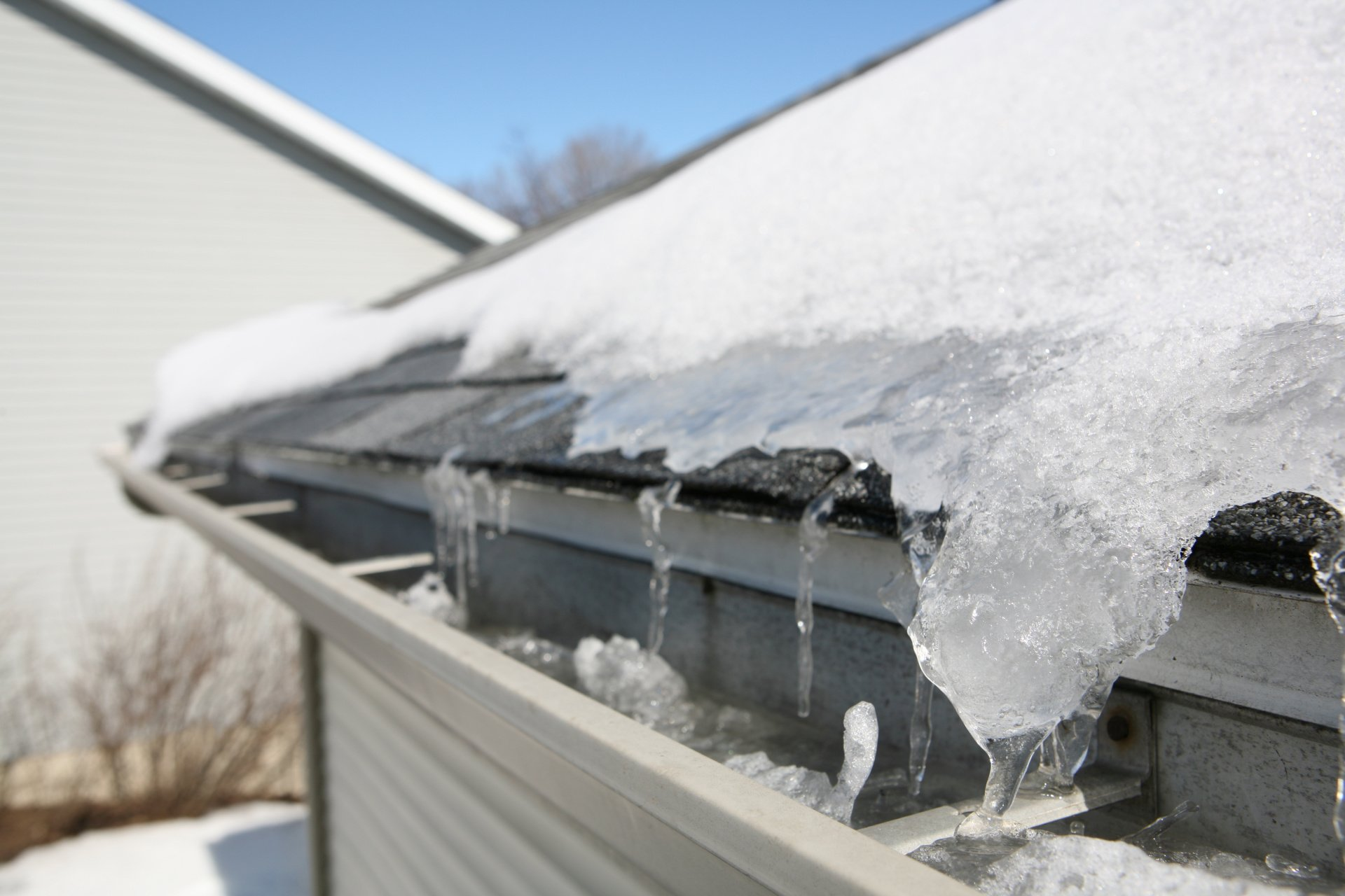 Snow and ice on a roof, melting into icicles over a gutter on a sunny day.