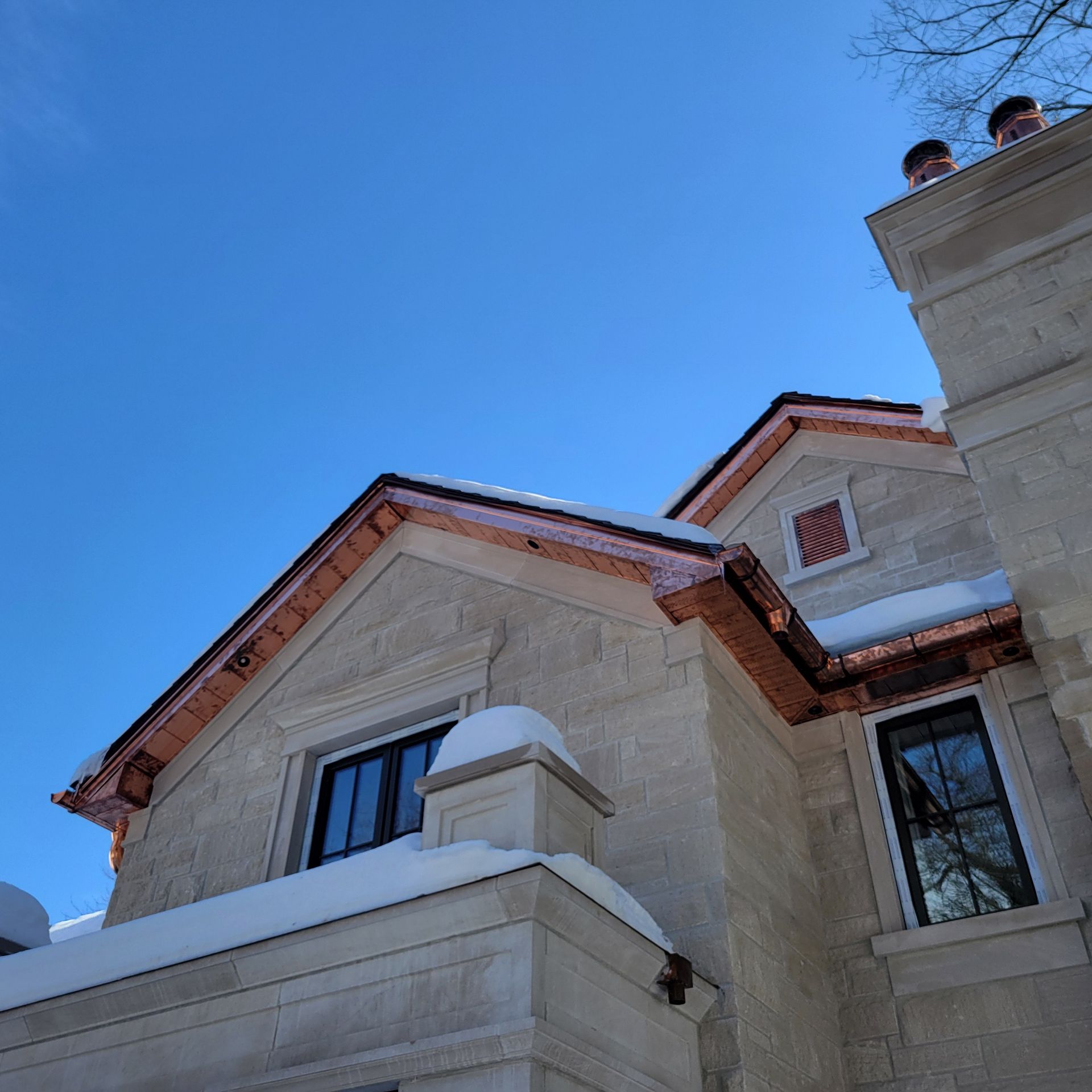 Stone building with copper roof trim, snow, and blue sky.