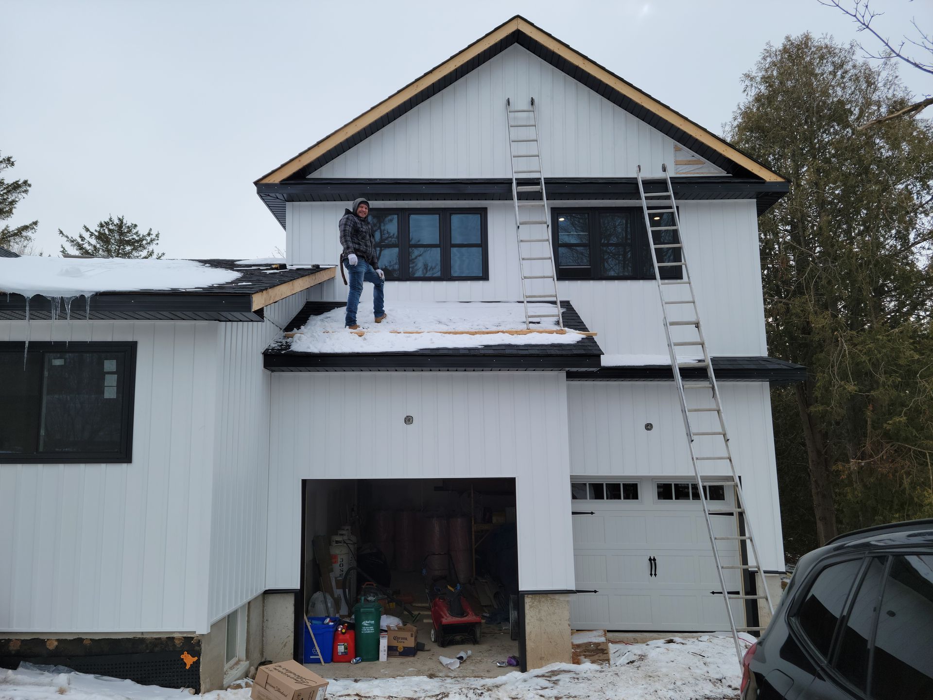 A construction worker on a snowy roof, installing black trim on a white house with black windows.