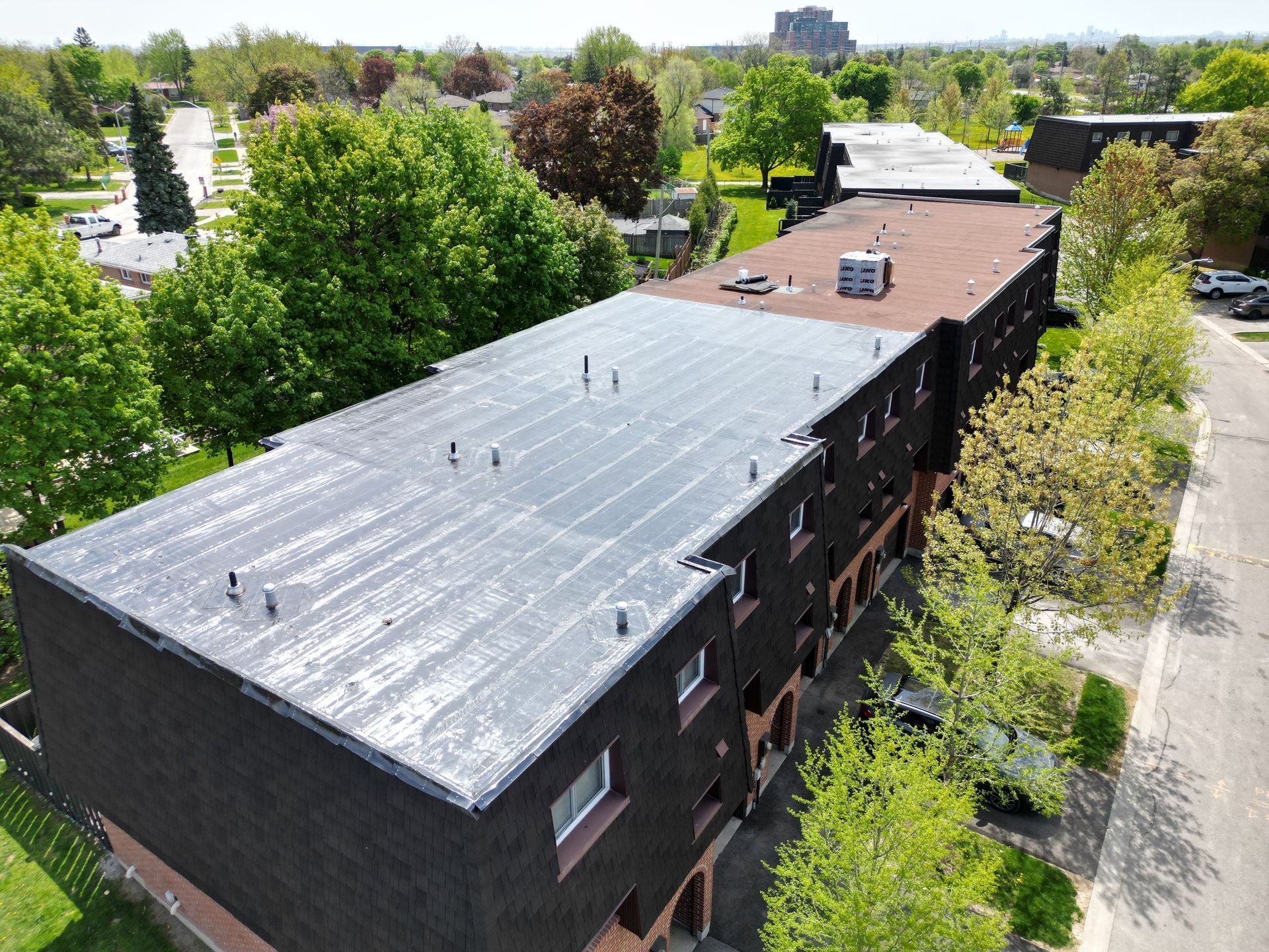 Aerial view of a flat, dark-roofed brick building in a residential area with green trees and streets.