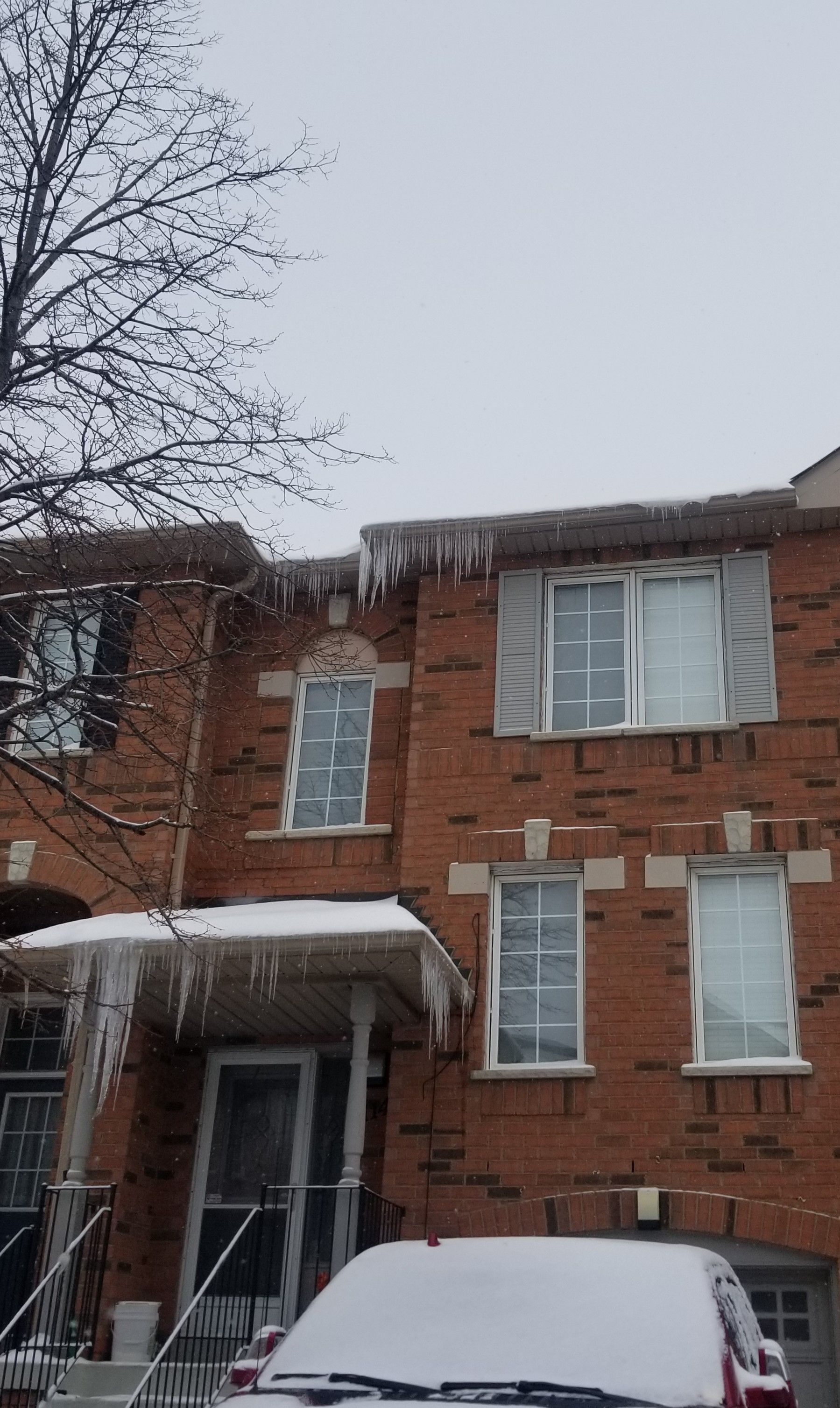 Brick townhouses with icicles hanging from the roof in winter. Snow covers the ground and car.