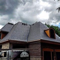 A large brick house with a gray roof and a van parked in front of it.