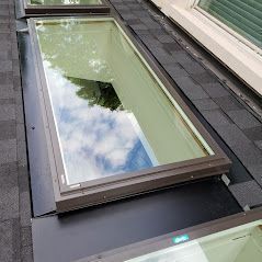A skylight is sitting on top of a roof next to a window.