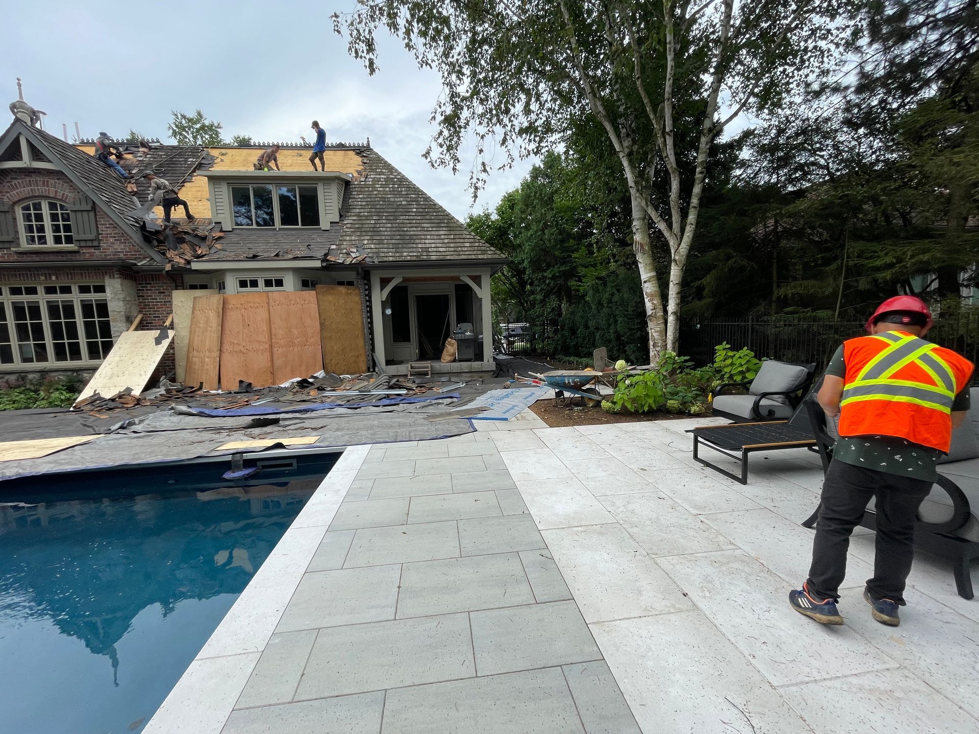 A man in an orange vest is standing next to a pool in front of a house being remodeled.
