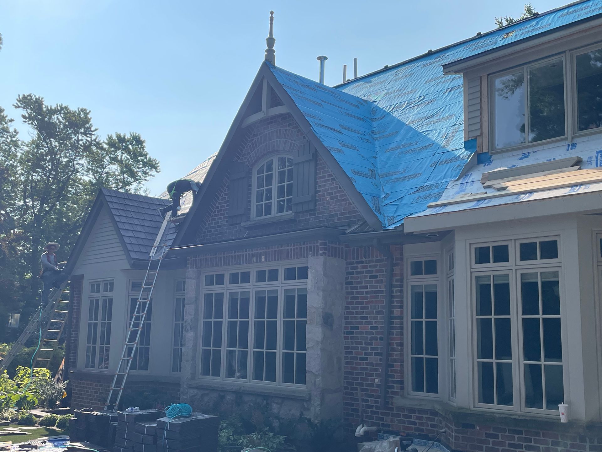 A large brick house with a blue tarp on the roof.