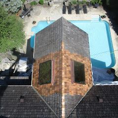Overhead view of a house roof with a partially cleaned area, two windows, and a blue swimming pool in the background.