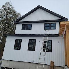 A white house with a black roof and a ladder on the side of it.