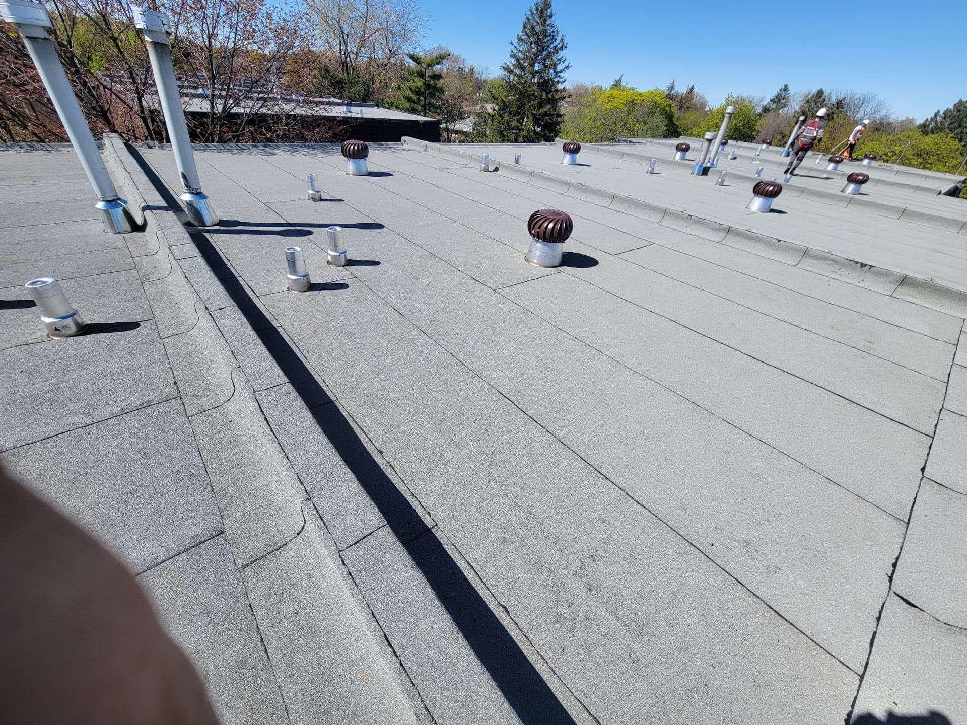 A flat, grey commercial roof under a clear blue sky, featuring multiple ventilation pipes and turbine vents.