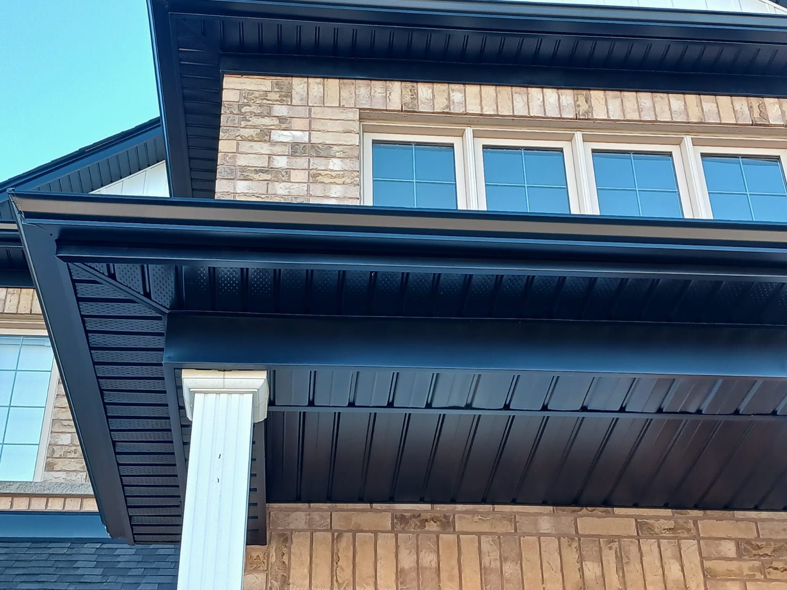 Brick home exterior with dark trim and gutters, white columns, and windows.