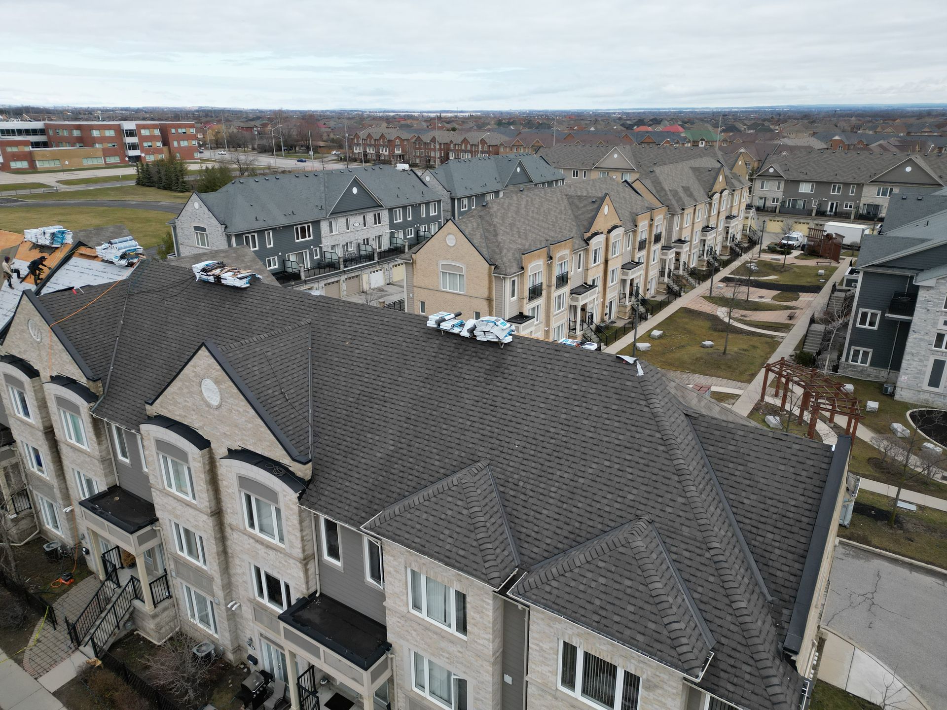 Aerial view of a row of townhouses with gray shingle roofs on an overcast day.