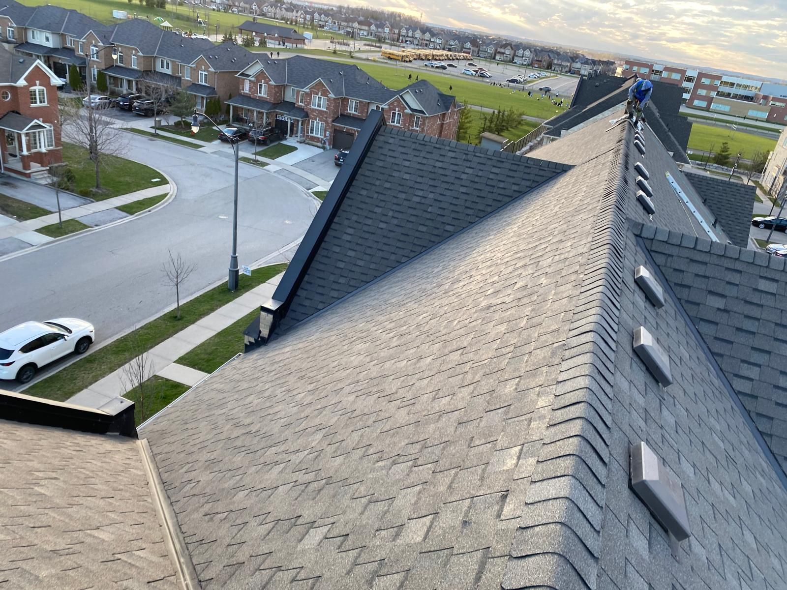 Rooftop view of a shingled roof with a person working, overlooking a suburban neighborhood.