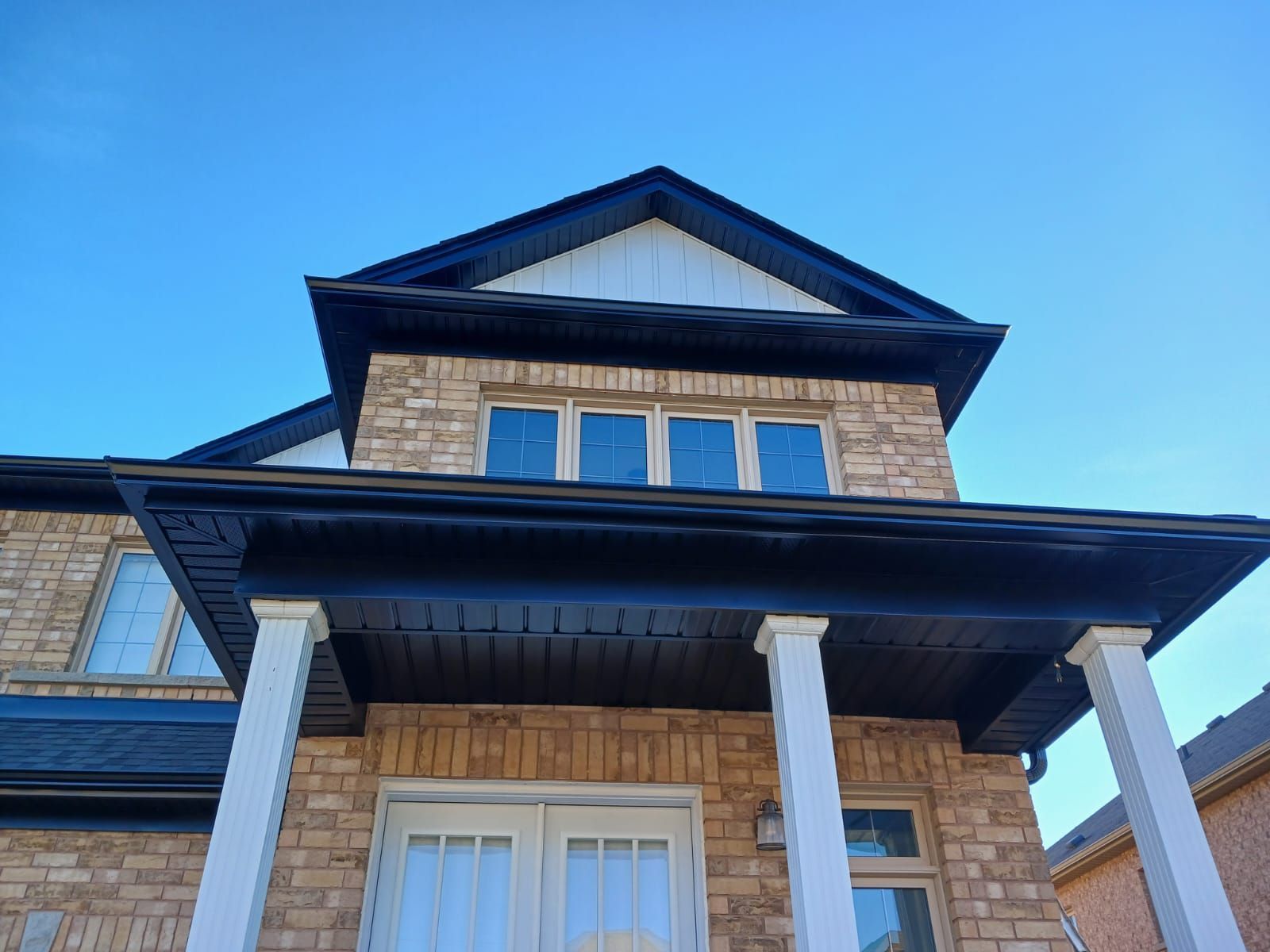 Two-story brick house with black trim, white columns, and a bright blue sky background.