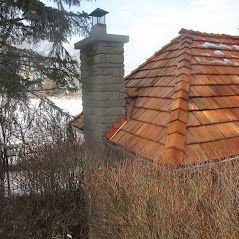 There is a chimney on the side of a house with a wooden roof.