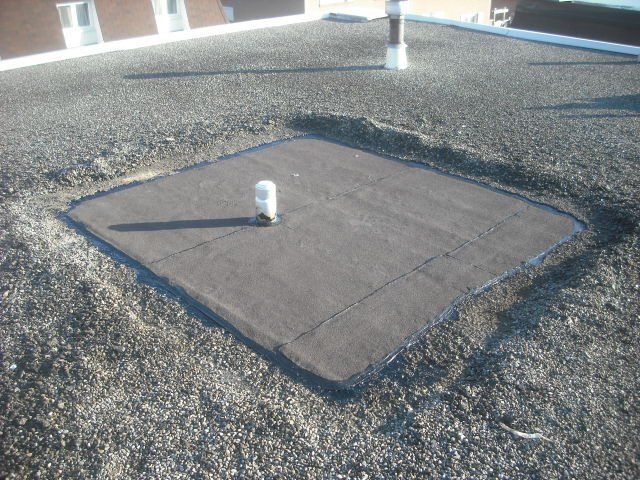 A square hole in the ground with a white pipe in it