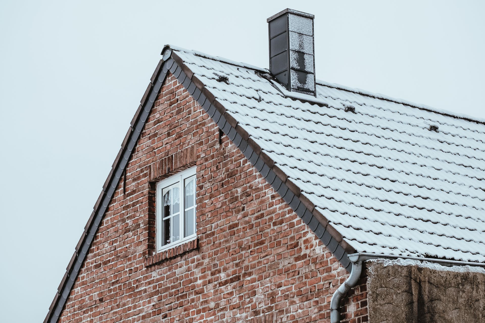 A brick house with a snowy roof and a window.