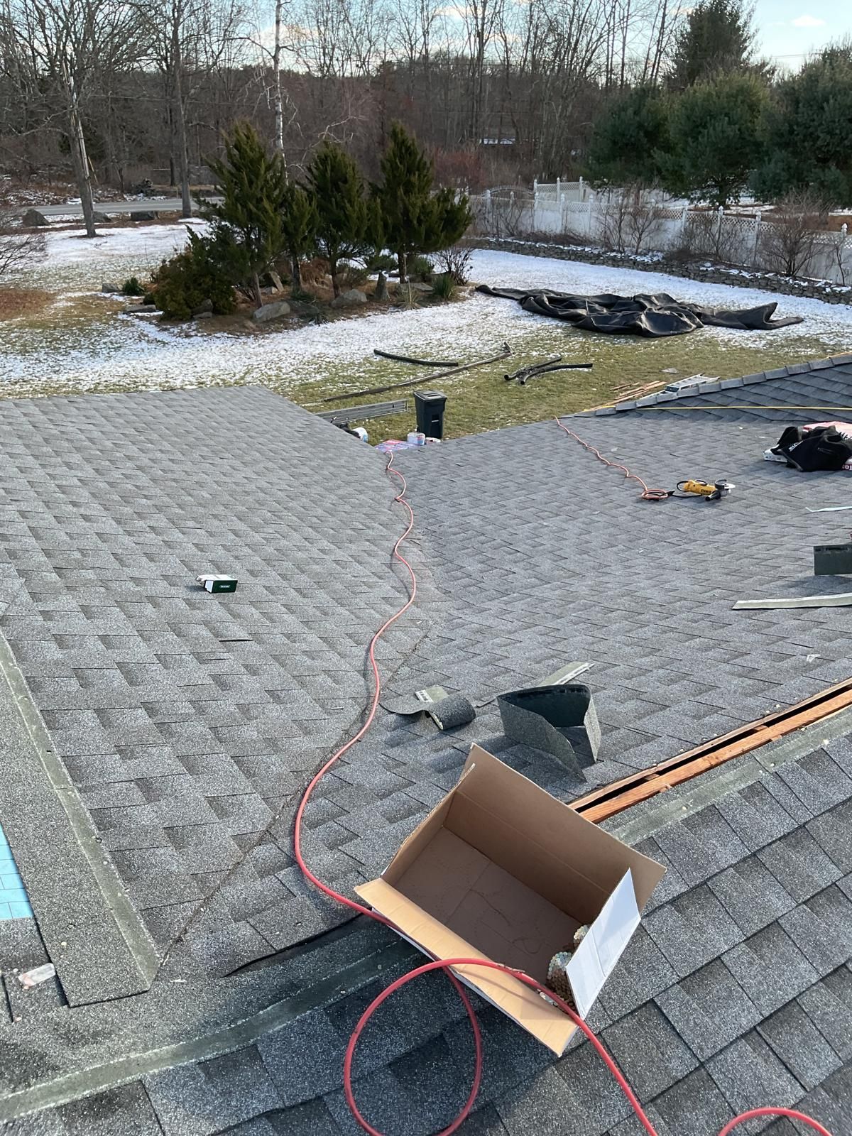 A partially shingled roof under construction with an open cardboard box and orange power cord on the surface.