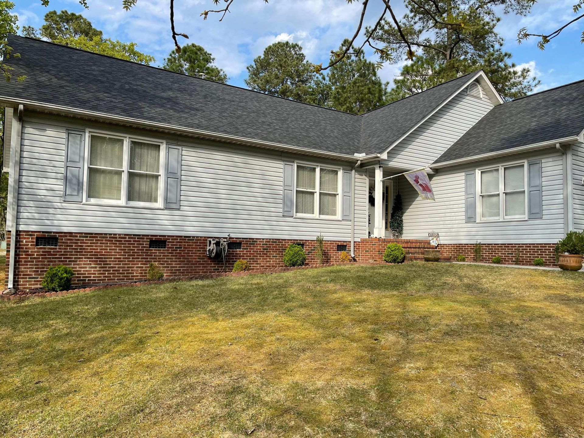 A white house with a black roof and shutters is sitting on top of a lush green lawn.